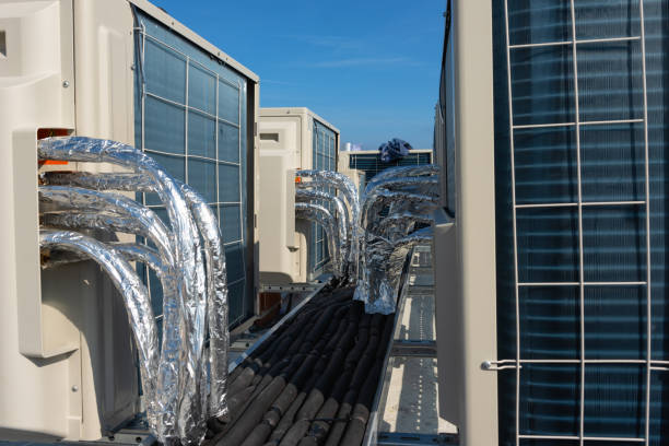 Air conditioner units (HVAC) on a roof of new industrial building with blue sky and clouds in the background.