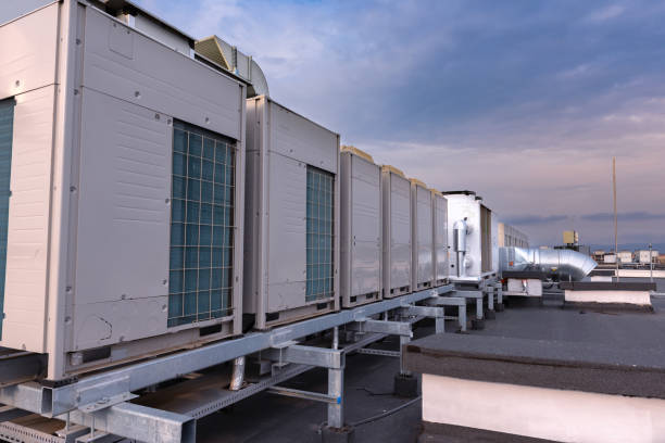 Air conditioner units VRV (HVAC), big fan and a water cooler on a roof of new industrial building with blue sky and clouds in the background.