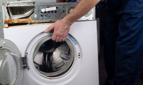 Repair of washing machines, repair of large household appliances. Repairman disassembles a washing machine for parts