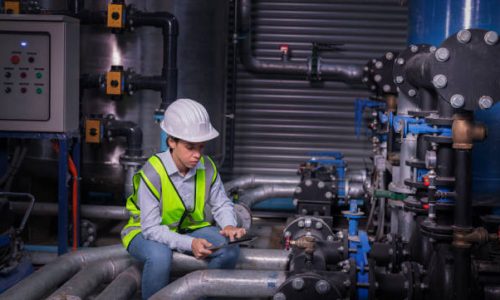 Industry engineer worker wearing safety uniform under checking the industry cooling tower air conditioner is water cooling tower air chiller HVAC of large industrial building to control air system.