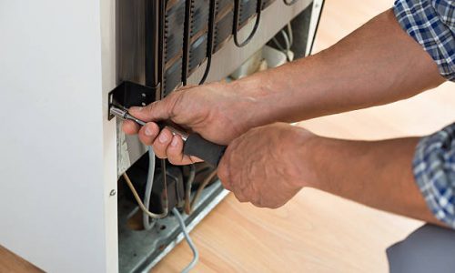 Cropped image of serviceman working on fridge with screwdriver at home