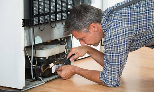 Cropped image of serviceman working on fridge with screwdriver at home